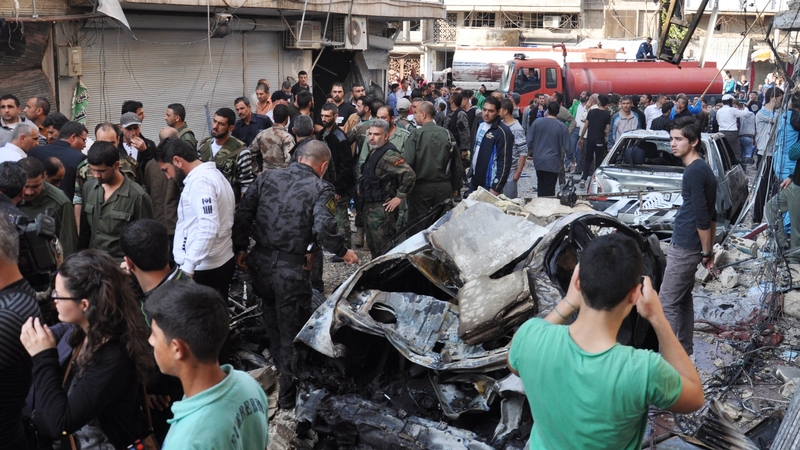 Syrian civilians and security forces stand at the site of a car bomb explosion in Homs