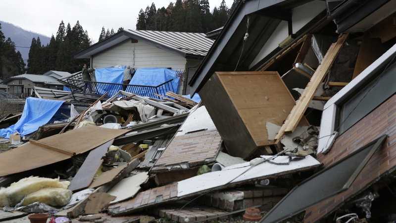 Residents cover pieces of their damaged home with plastic to protect it from snow