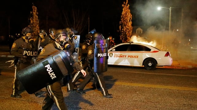 Police in Ferguson walk past a burning car as demonstrators protest the grand jury decision