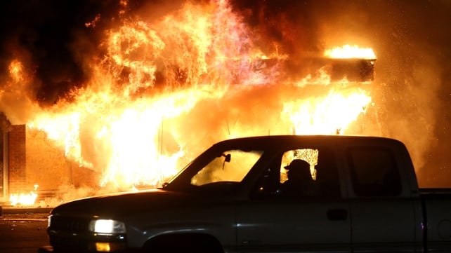 A car is driven past a burning building during the riots in Ferguson