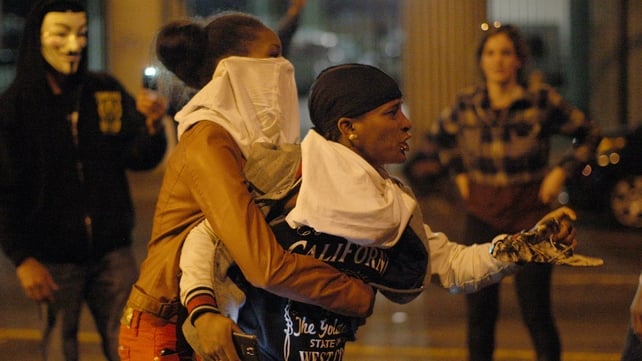 A protester in Los Angeles is restrained from running toward police after being hit with a less lethal round