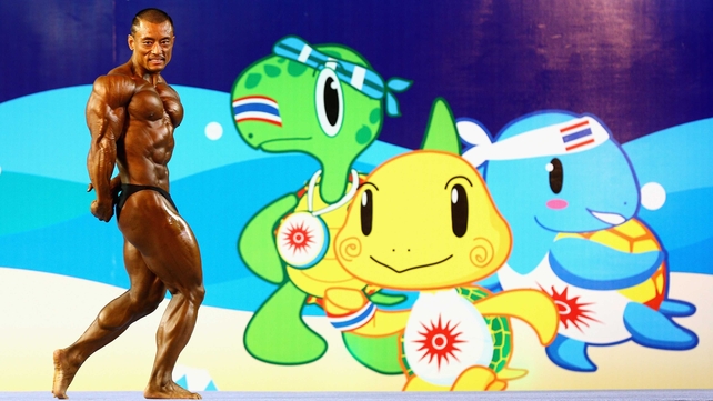 China's Xin Jian poses in front of Asian Beach Games mascots Sakorn, Sintu and Samut as he competes in the open weight category bodybuilding competition