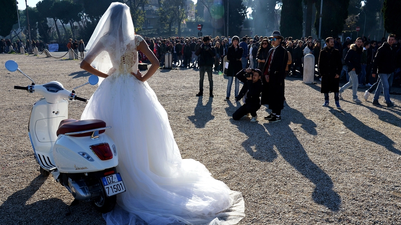 A bride poses in front of a Vespa motorbike in the Circo Massimo in Rome, as people in the background take part in a strike over the budget