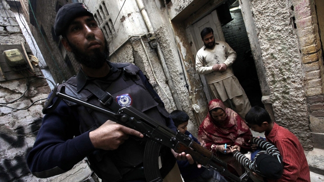 A member of the Pakistani security services stands guard while a health worker administers a polio vaccine to a child