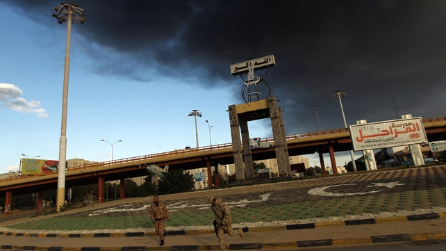Members of the Libyan army in Benghazi run as heavy black smoke rises from the city's port in the background