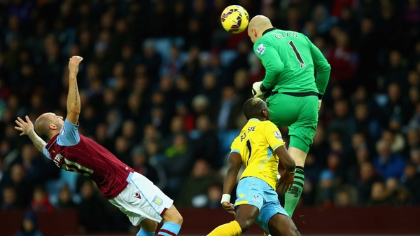Aston Villa goalkeeper Brad Guzan heads the ball under pressure from Yannick Bolasie