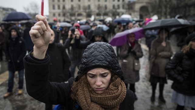 A young woman holds a symbol as she joins others gathered for a minute's silence in front of Notre Dame cathedral
