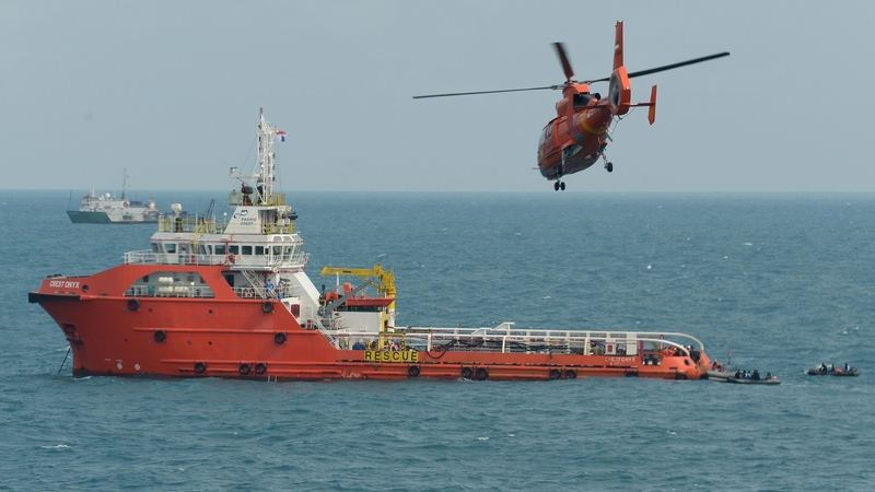 A rescue helicopter flies over Crest Onyx as divers conduct operations to lift the tail of the air craft