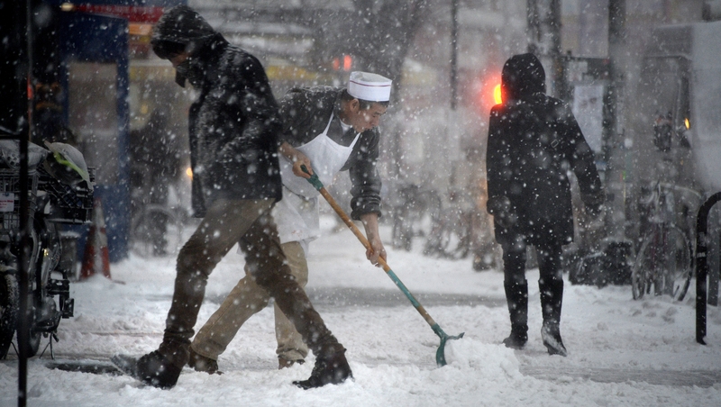 A man shovels snow from a pavement as the storm arrives in New York