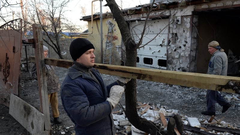 Local residents repair a fence next to their partially-destroyed home in Donetsk