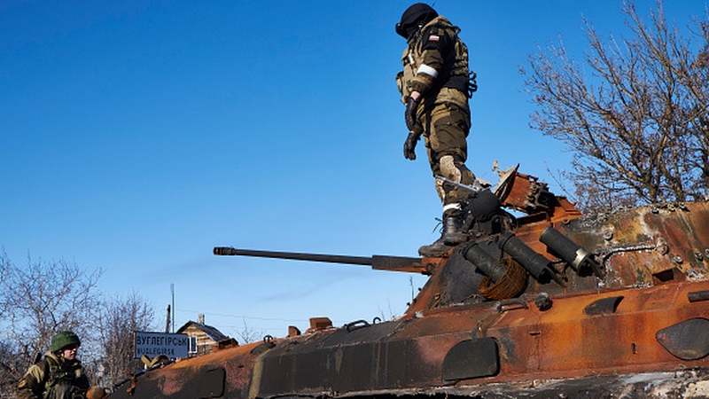 A pro-Russian rebel stands on top of a destroyed Ukrainian armored vehicle
