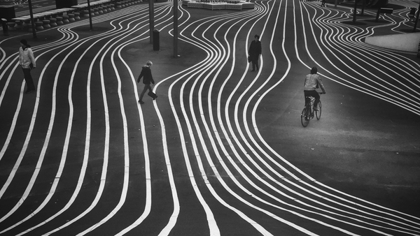 The photo captures twisting white lines on a pavement as four people walk upon it