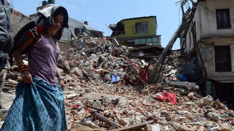 A woman walks past a damaged house in Balaju in Kathmandu
