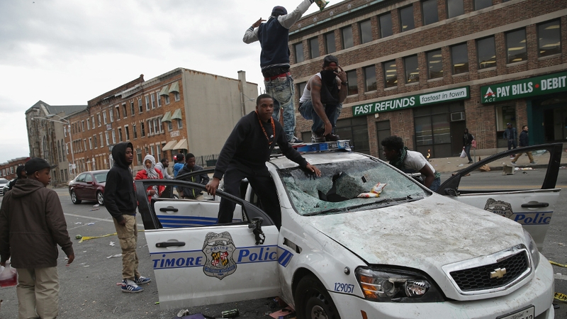 Young men climb on a destroyed Baltimore police car during yesterday's violent protests