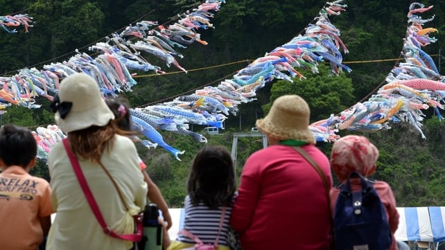 Holidaymakers have a picnic near carp streamers fluttering above a riverside park in Sagamihara, suburban Tokyo