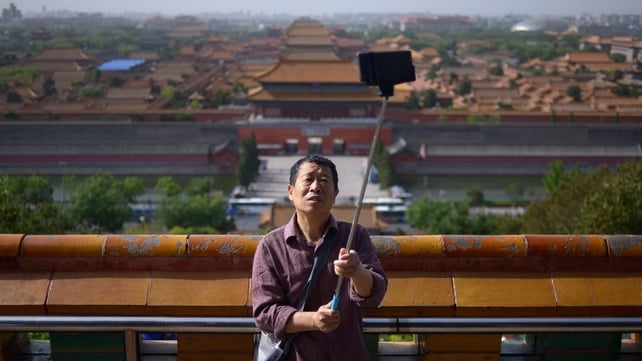 An elderly man uses a selfie stick to take a photo at a park near the Forbidden City in Beijing