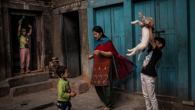 A young boy tosses his puppy as he plays with other children outside his home in Kathmandu, Nepal