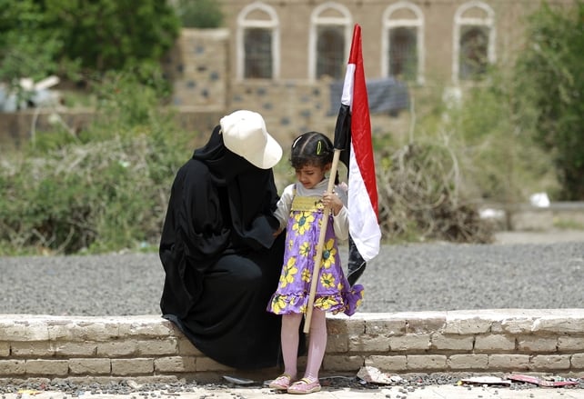 Yemeni woman and child holding her national flag rest on wall during a rally protesting against the Saudi-led airstrikes