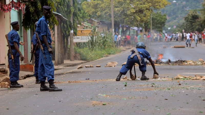 Police officers removing rocks from a barricade set up by protesters as they face them in the capital Bujumbura