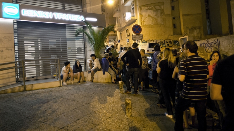 People queue in front of an ATM mache to withdraw cash from a National Bank of Greece in central Athens