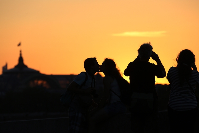 Lovers kiss while tourists take a picture of Paris monuments, at sunset