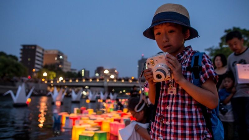 A young boy takes photographs after placing a candle lit paper lantern on the river at the Hiroshima Peace Memorial Park
