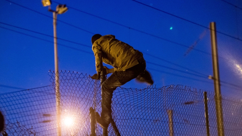A migrant climbs a fence to enter the Channel Tunnel site