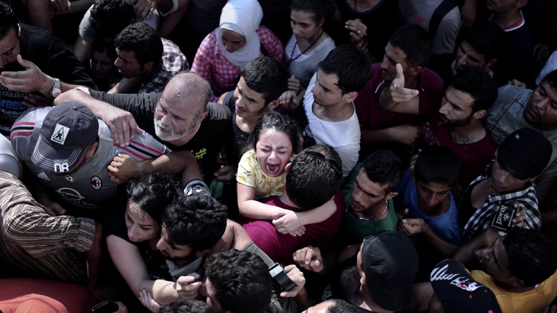 A young child cries as people are tightly packed in a queue for immigration papers