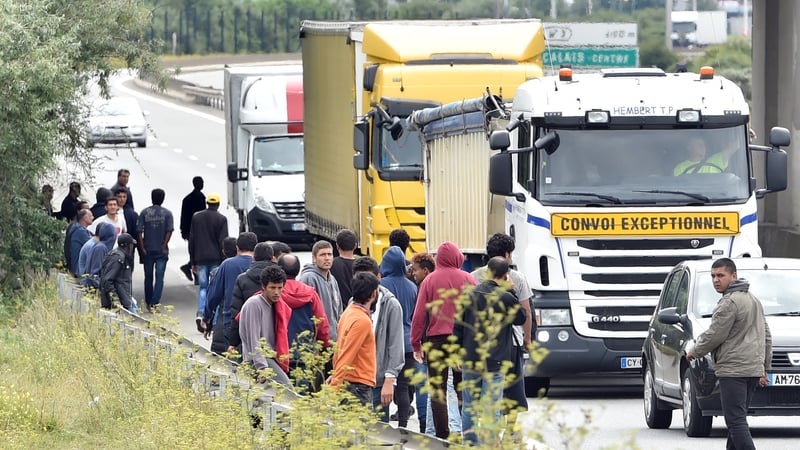 Migrants stand as lorries drive past on the road leading to the ferry port in Calais