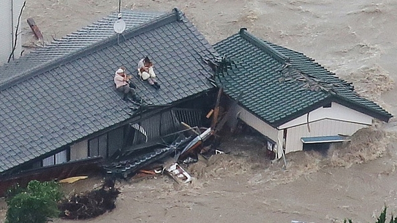 Local residents wait to be rescued on the roof of their home in a flooded area in Joso