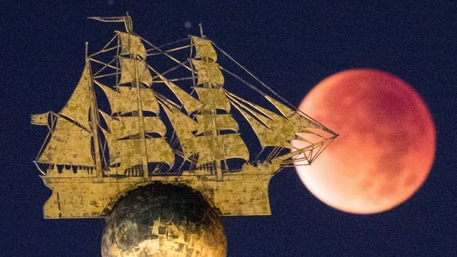 The supermoon appears red behind the sculpture of a sailing ship in Hamburg, Germany