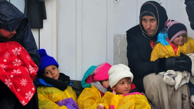 A migrant family sit on the ground in the rain at the closed crossing in Trnovec, Croatia