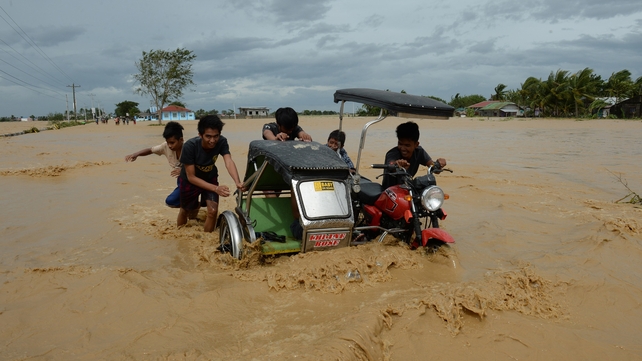 Residents push a tricycle on a flooded highway in Santa Rosa, north of Manila