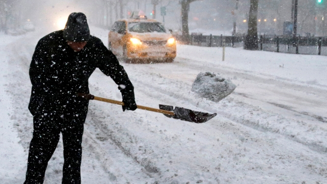 A man moves snow off the street as a New York City taxi drives by on the Lower East Side of Manhattan