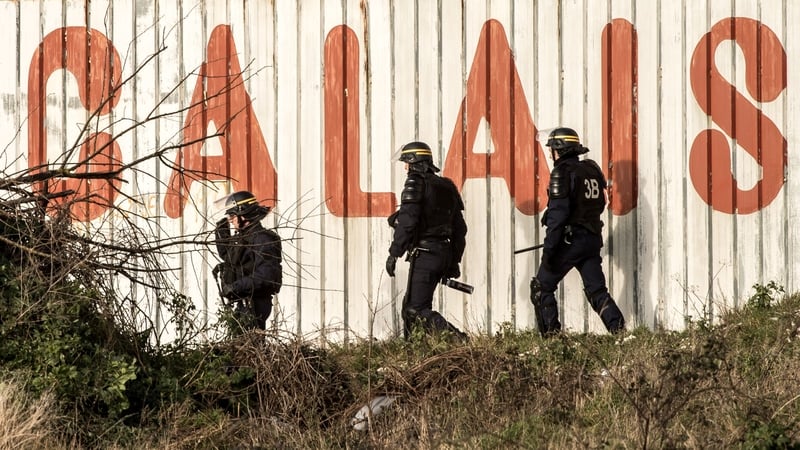 French riot police officers walk in front of a fence near the site of the Eurotunnel