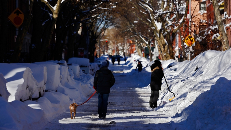 A man walks his dog as a woman shovels out a car in the Brooklyn borough of New York City