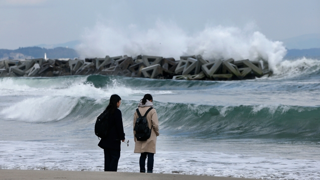 People stand with flowers on the shore to offer a prayer for victims at tsunami-devastated Abraham, a coastal district of Sendai