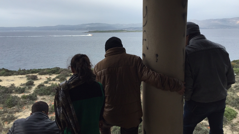 People gaze across the narrow strait of water separating Turkey from the Greek island of Chios, clearly visible on the horizon