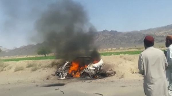 Onlookers survey the burning wreckage of the vehicle Mansour was travelling in when it was attacked by a US drone