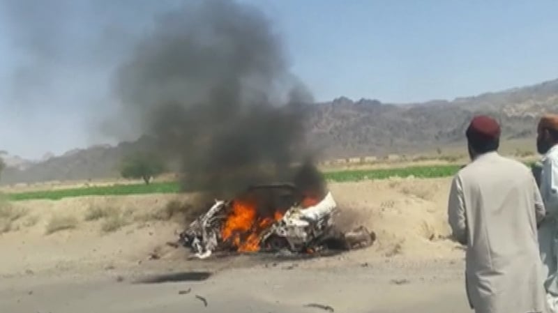 Onlookers survey the burning wreckage of the vehicle Mansour was travelling in when it was attacked by a US drone