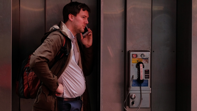 A man uses a mobile phone while standing at a pay phone in New York