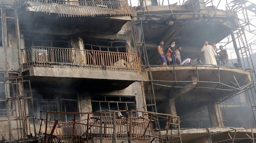 Iraqis look on as they inspect the site of a suicide car bomb attack in the Karrada district of central Baghdad, Iraq