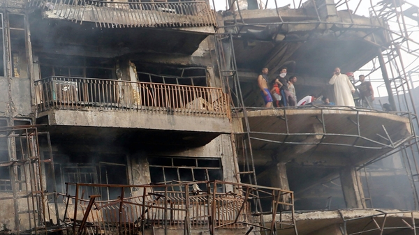 Iraqis look on as they inspect the site of a suicide car bomb attack in the Karrada district of central Baghdad, Iraq