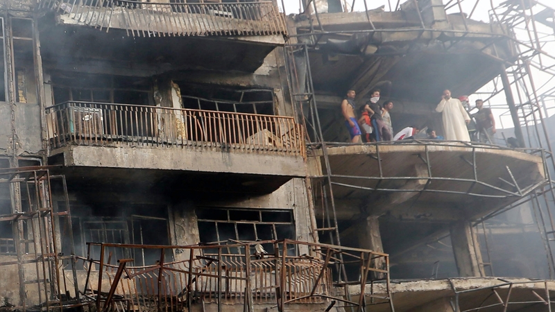 Iraqis look on as they inspect the site of a suicide car bomb attack in the Karrada district of central Baghdad, Iraq