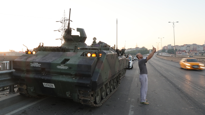 A man takes a 'selfie' against a military tank being guarded by Turkish police on the Bosphorus bridge