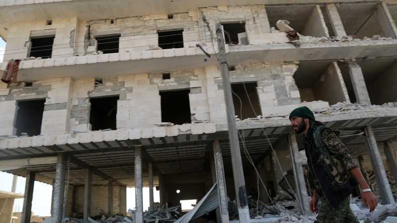 A member of the US-backed Kurdish and Arab fighters walks past destroyed buildings as they advanced into Manbij in June
