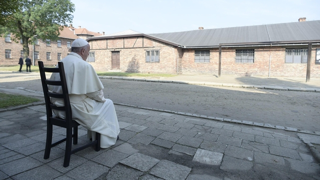 A photo provided by Vatican newspaper Osservatore Romano shows Pope Francis quietly reflecting as he sits in front of camp buildings
