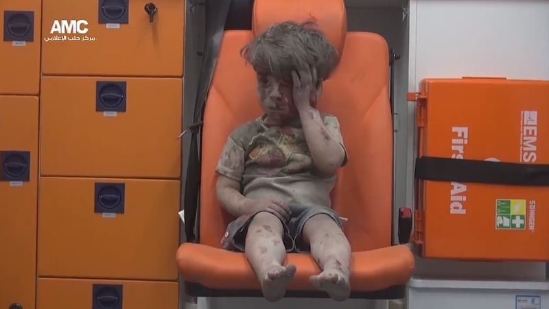 Omran Daqneesh is seen wiping blood off his head as he sits alone in an ambulance