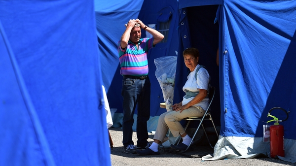 A couple wait outside a tent at a camp for displaced people in Pescara del Tronto