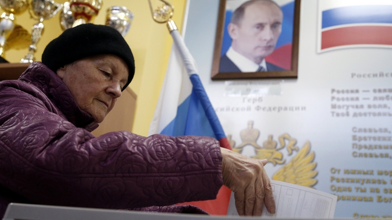 An elderly woman casts her ballot in front of a portrait of Russian President Vladimir Putin at a polling station in Moscow, Russia